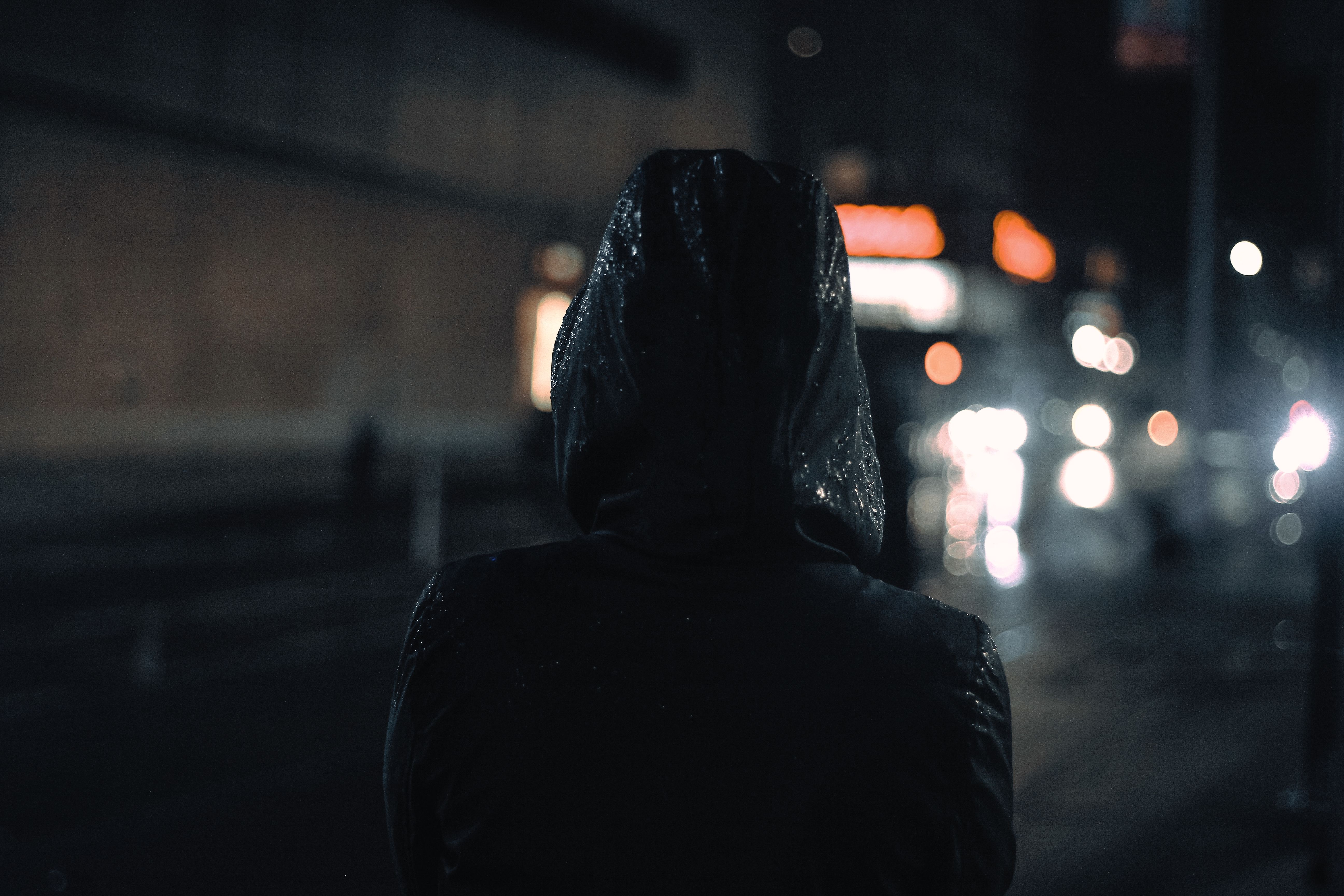 A hooded figure walking through a city at night, representing anonymity in the digital age.
