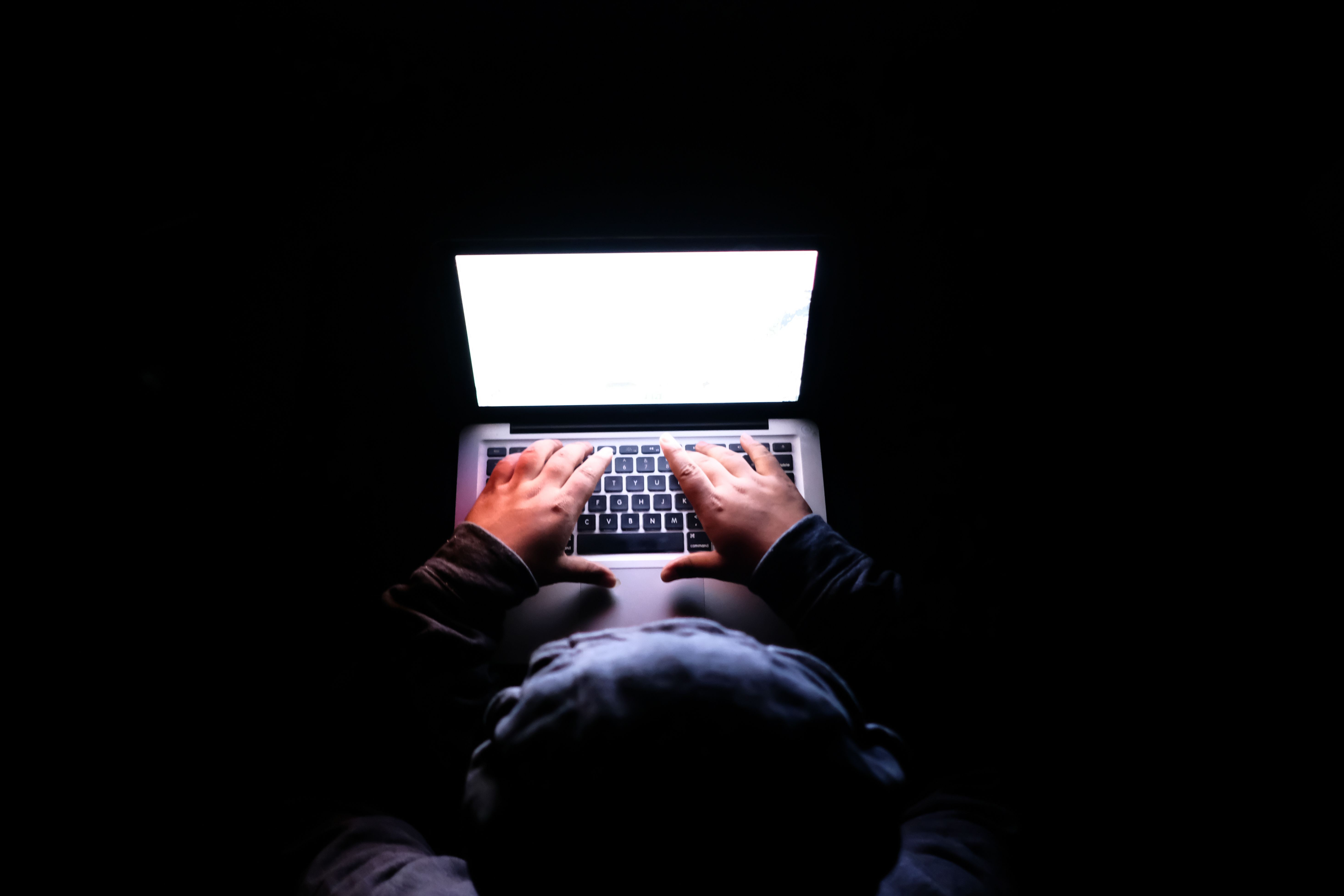 A person typing on a laptop in a dark room, evoking confidential work and online privacy.